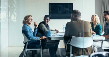 Men and women sitting down in a meeting looking at each other and smiling.